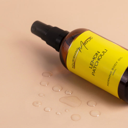 Nourishing Mana Lemon Patchouli Morning Body Oil in a 100ml amber glass spray bottle with oil droplets on a beige background.