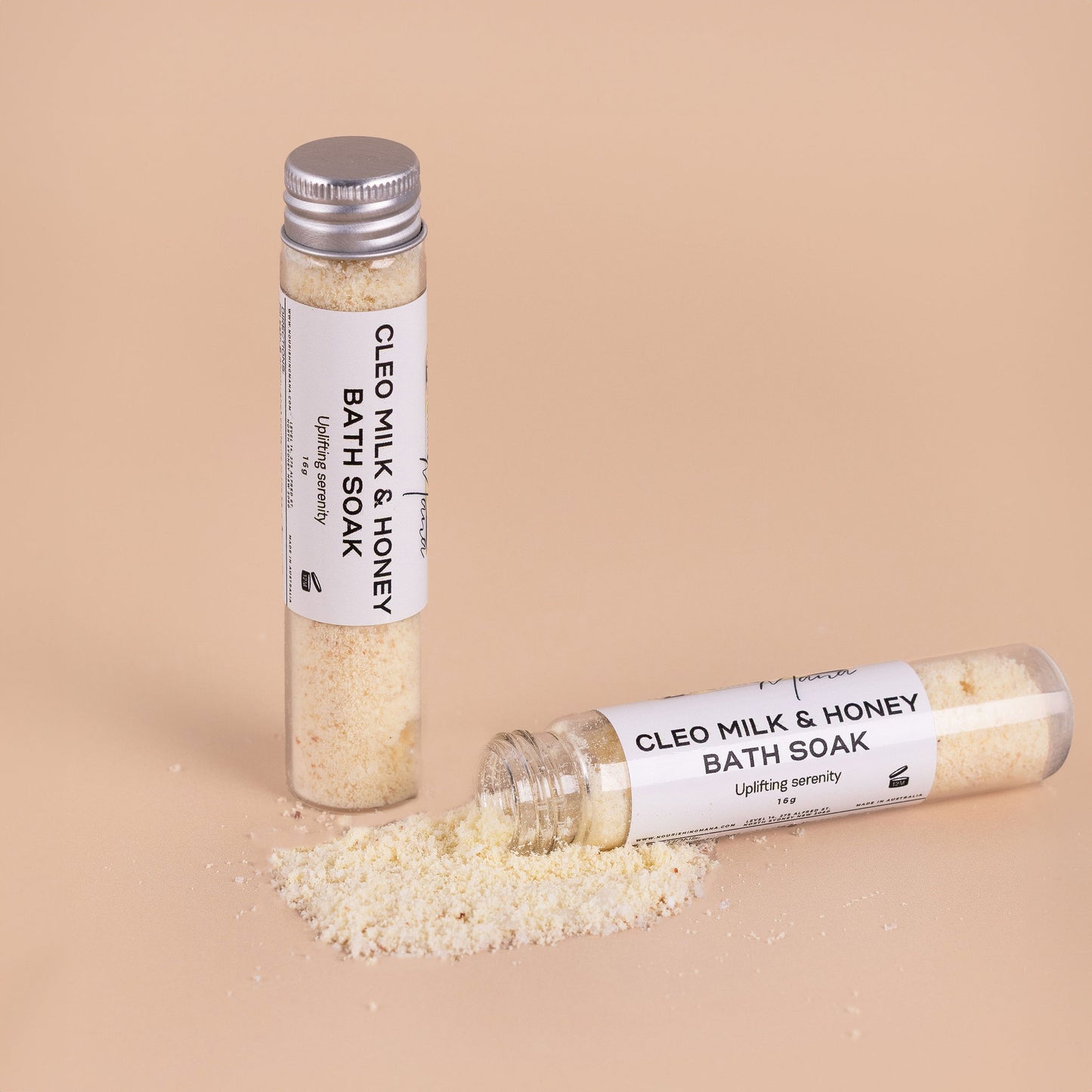 Nourishing Mana Milk and Honey Bath Soak with petitgrain and bergamot in glass tubes with bath soak powder on a beige background.
