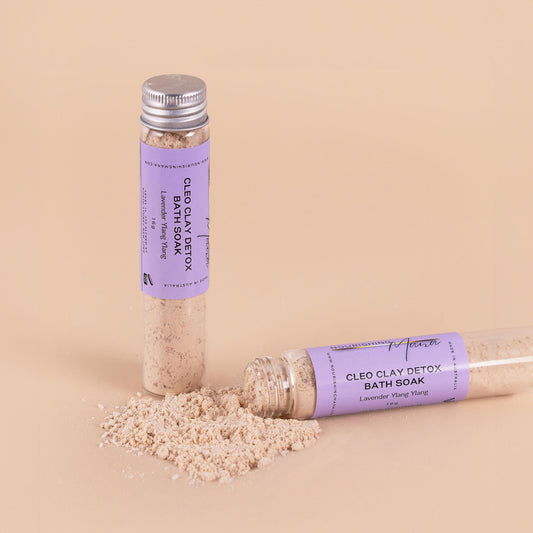 Nourishing Mana Cleo Clay Detox Bath Soak with lavender and ylang ylang in glass tubes with mineral-rich bath soak powder on a beige background.