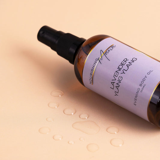 Nourishing Mana Lavender Ylang Ylang Evening Body Oil in a 100ml amber glass spray bottle with oil droplets on a beige background.