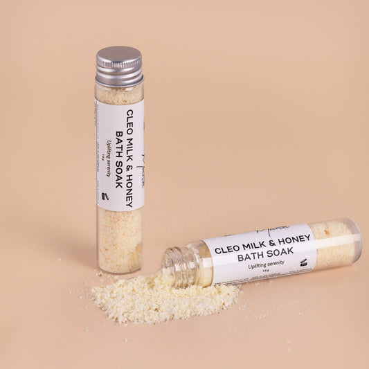 Nourishing Mana Milk and Honey Bath Soak with petitgrain and bergamot in glass tubes with bath soak powder on a beige background.