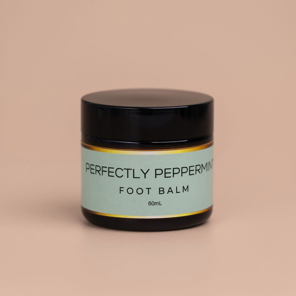 Nourishing Mana Perfectly Peppermint Foot Balm in a 60ml amber glass jar with a black lid on a beige background.