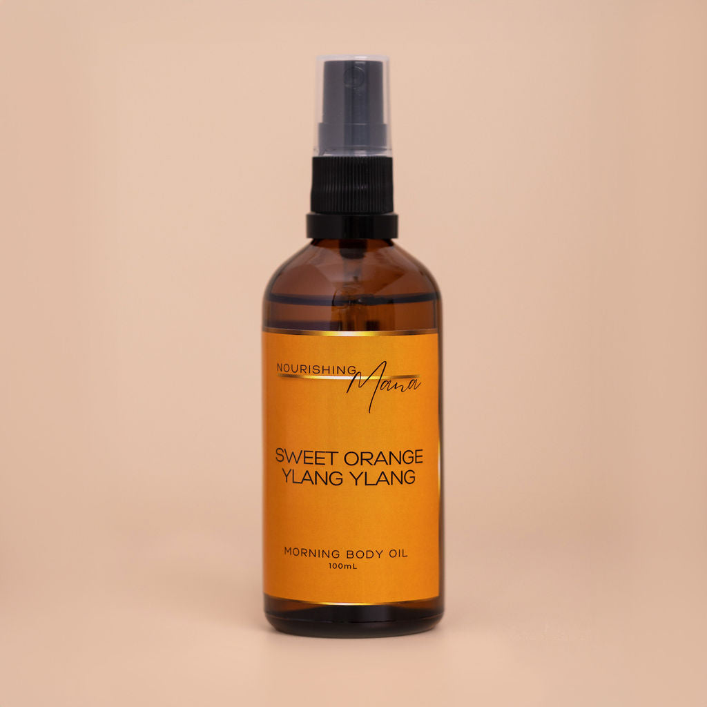 Nourishing Mana Sweet Orange Ylang Ylang Morning Body Oil in a 100ml amber glass spray bottle on a beige background.