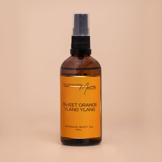 Nourishing Mana Sweet Orange Ylang Ylang Morning Body Oil in a 100ml amber glass spray bottle on a beige background.