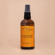 Nourishing Mana Sweet Orange Ylang Ylang Morning Body Oil in a 100ml amber glass spray bottle on a beige background.